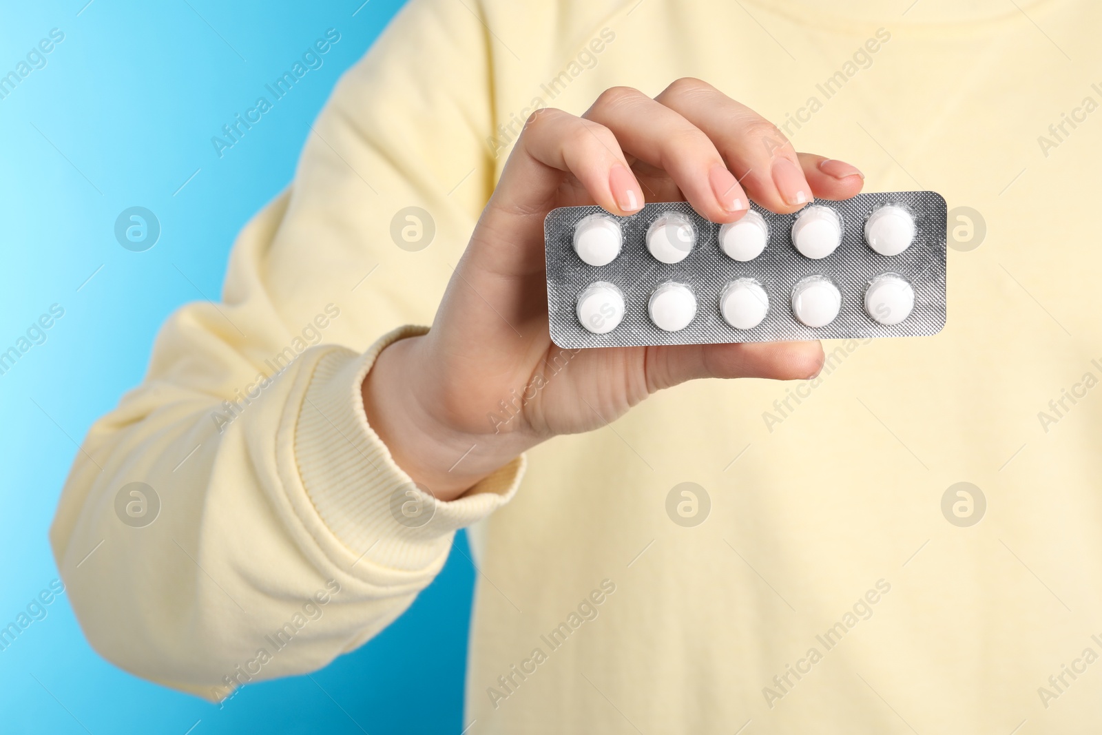 Photo of Woman holding blister with antibiotic pills on light blue background, closeup