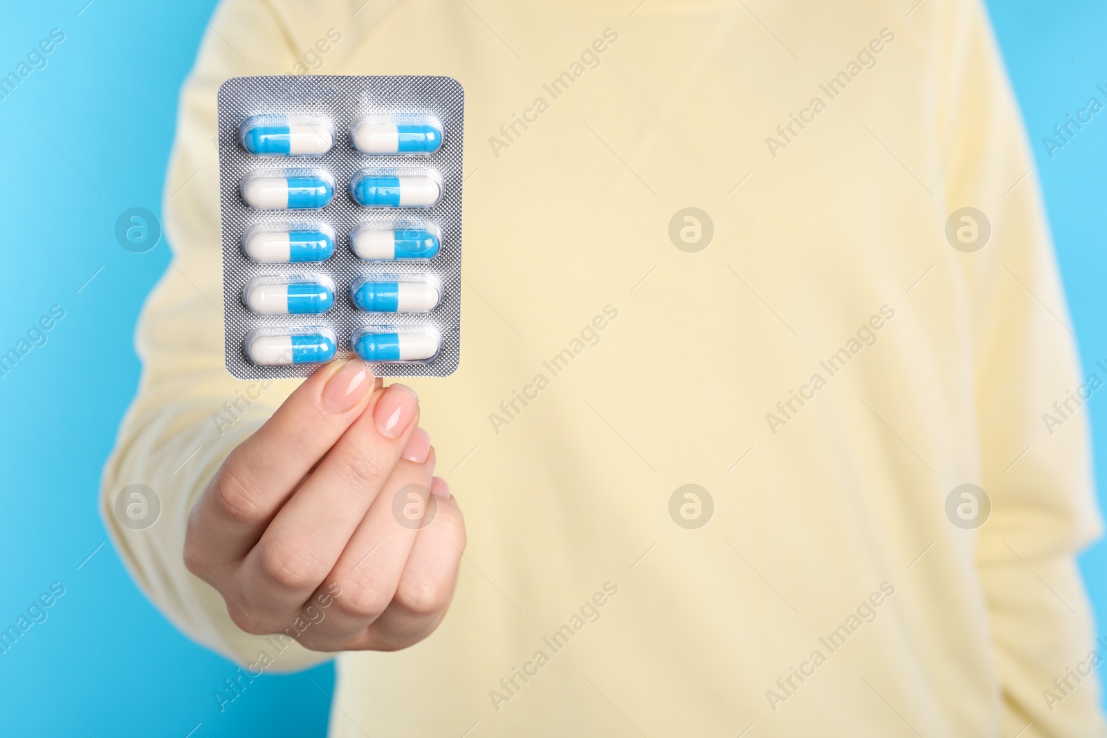 Photo of Woman holding blister with antibiotic pills on light blue background, closeup