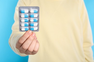 Woman holding blister with antibiotic pills on light blue background, closeup