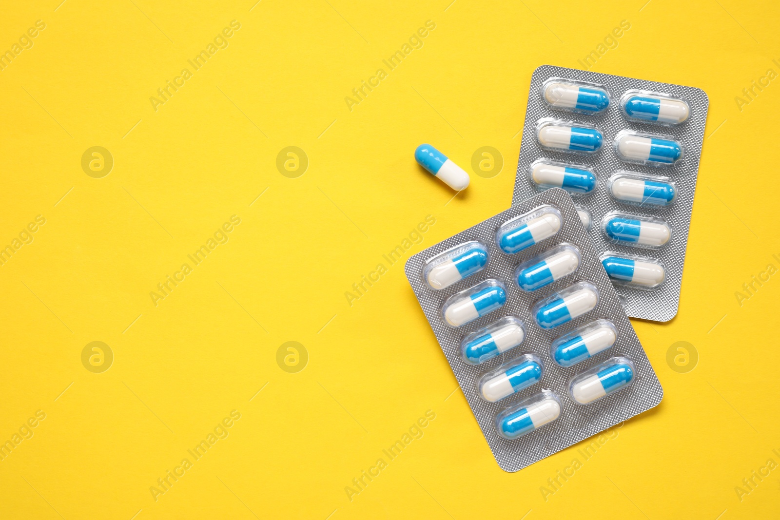 Photo of Antibiotic pills in blisters on yellow background, top view. Space for text