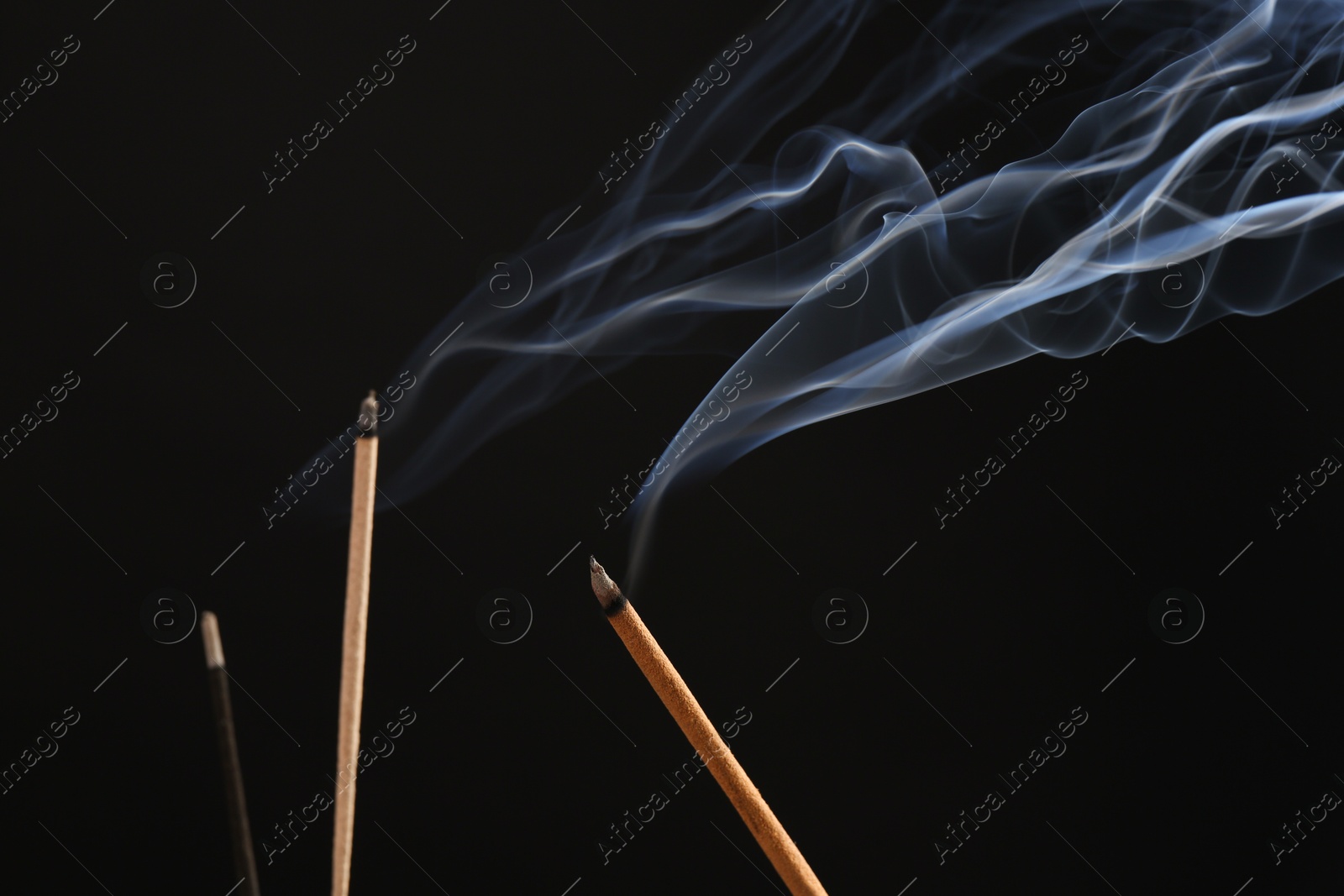 Photo of Aromatic incense sticks smoldering on black background