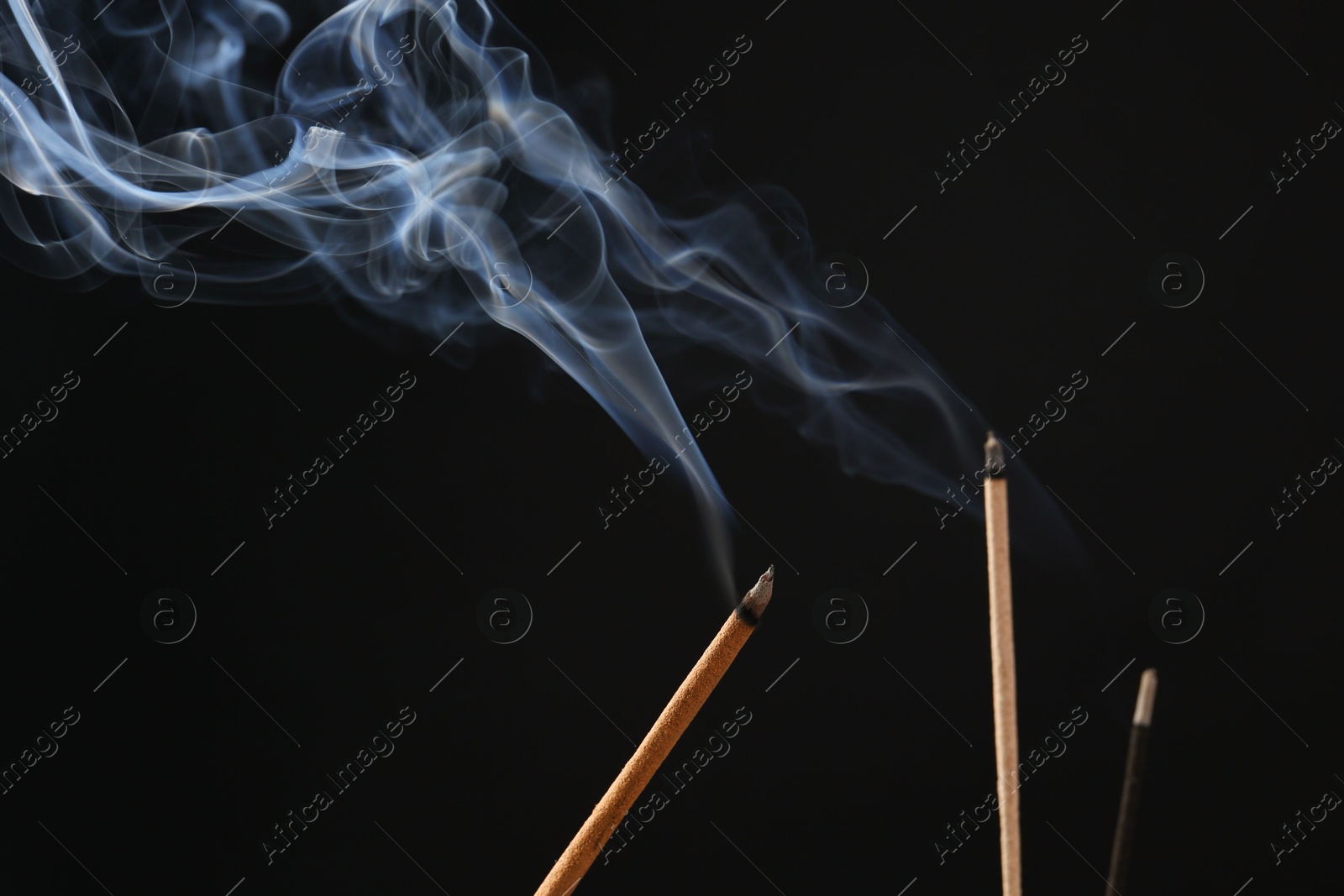 Photo of Aromatic incense sticks smoldering on black background