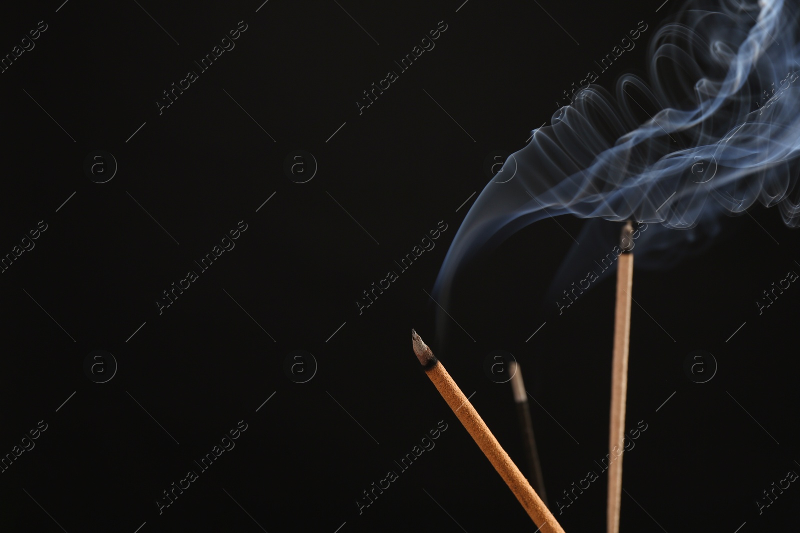 Photo of Aromatic incense sticks smoldering on black background. Space for text