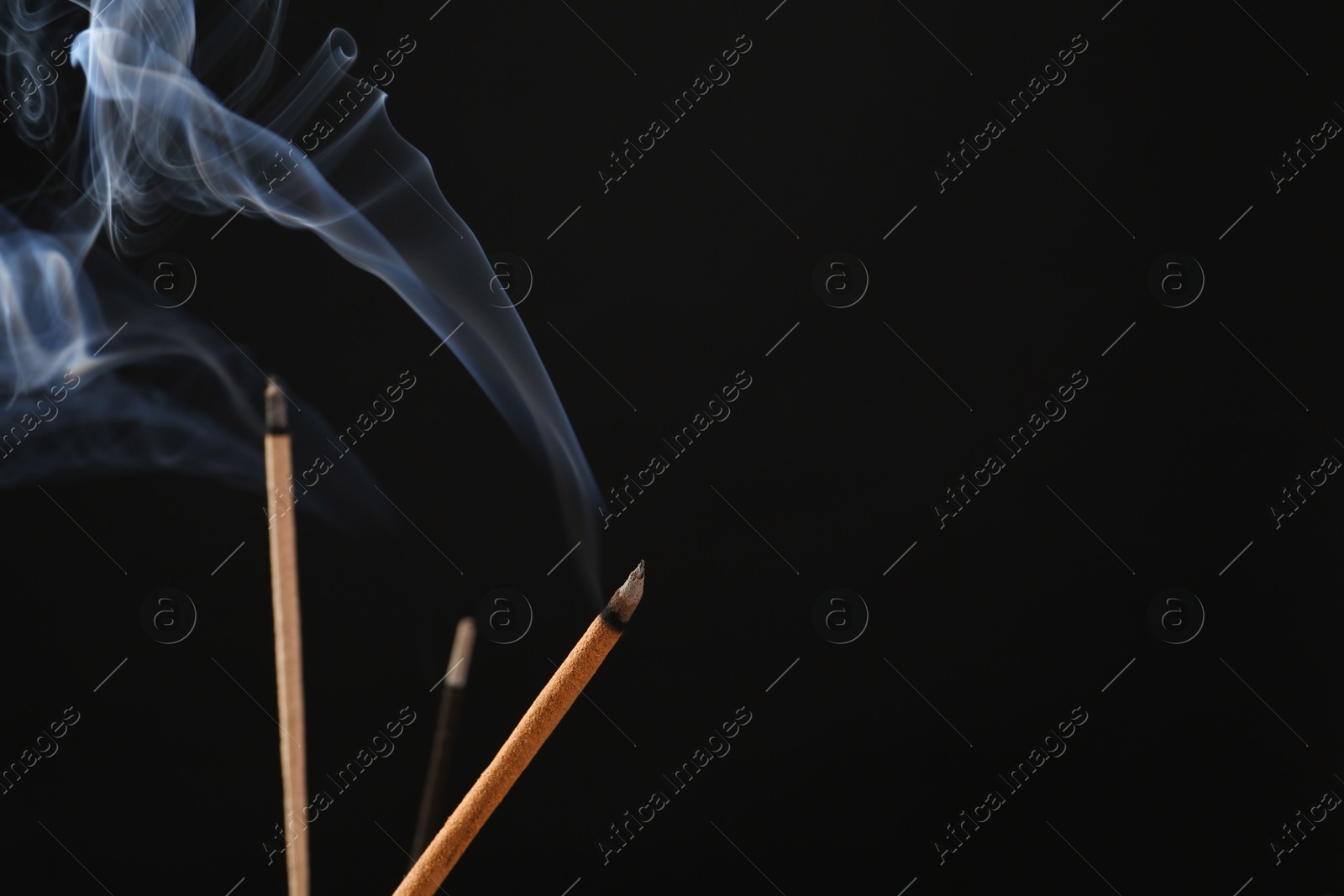 Photo of Aromatic incense sticks smoldering on black background. Space for text