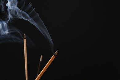 Photo of Aromatic incense sticks smoldering on black background. Space for text