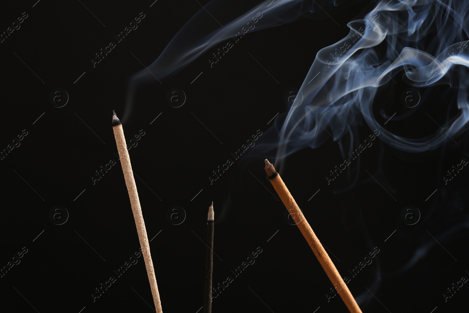 Photo of Aromatic incense sticks smoldering on black background