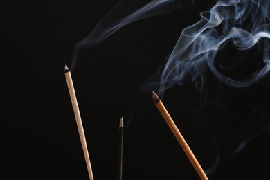 Aromatic incense sticks smoldering on black background