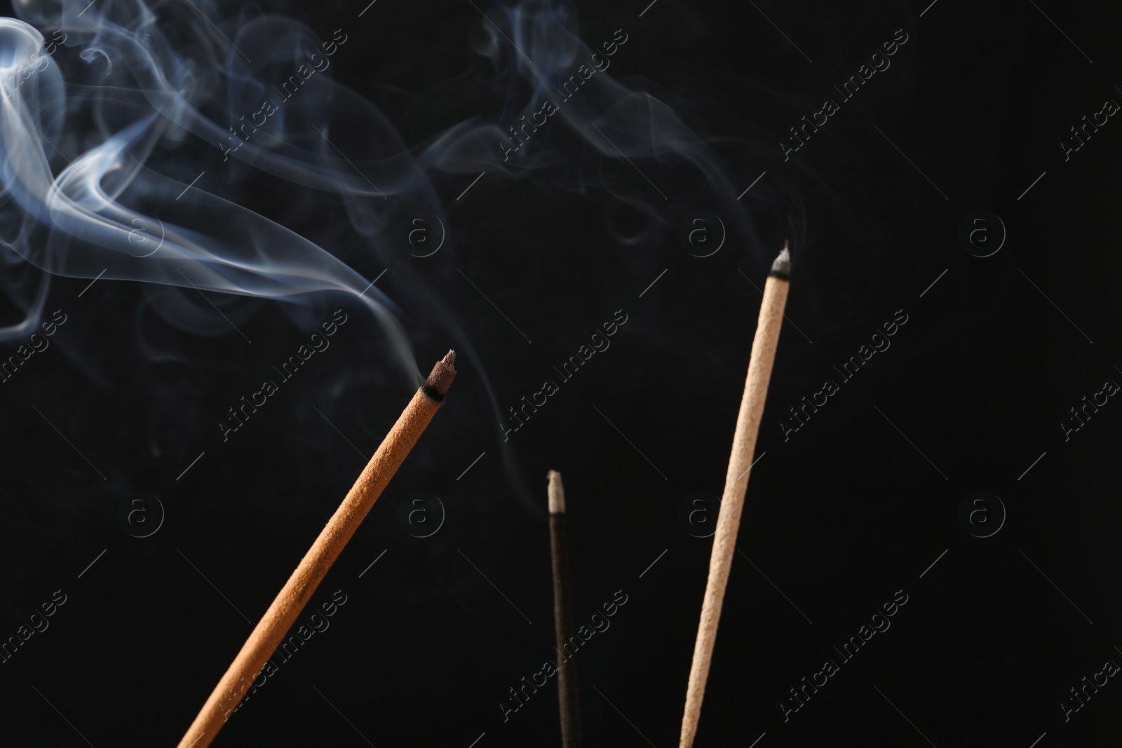 Photo of Aromatic incense sticks smoldering on black background