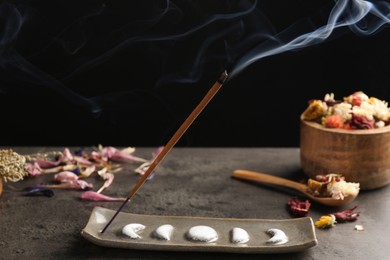 Aromatic incense stick smoldering on grey table