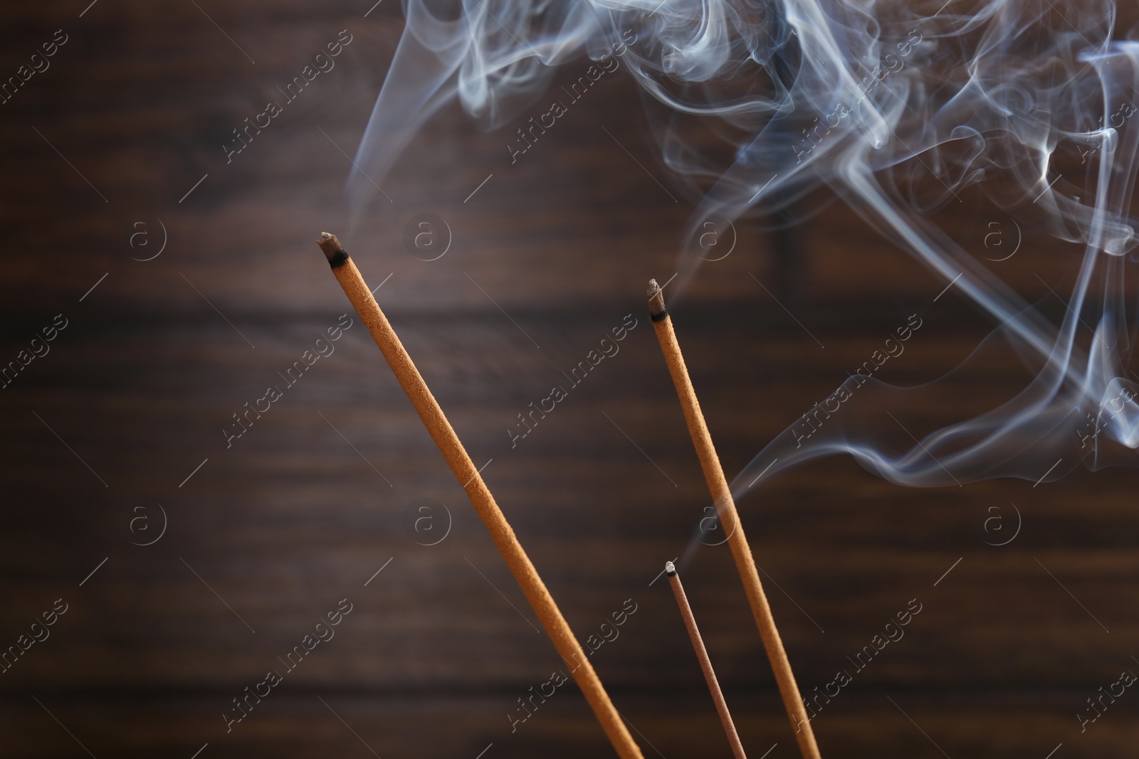 Photo of Aromatic incense sticks smoldering on blurred background, closeup