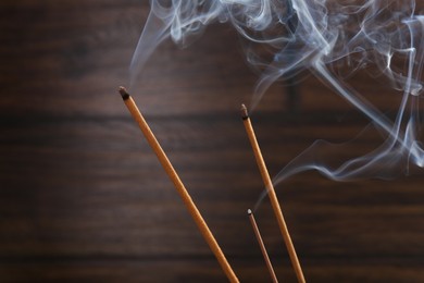 Photo of Aromatic incense sticks smoldering on blurred background, closeup