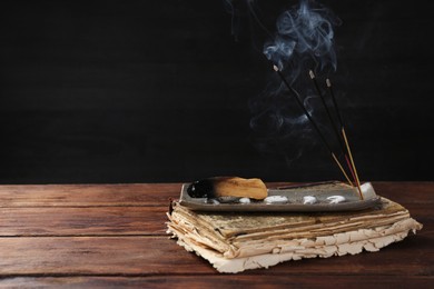 Photo of Aromatic incense sticks smoldering on wooden table. Space for text