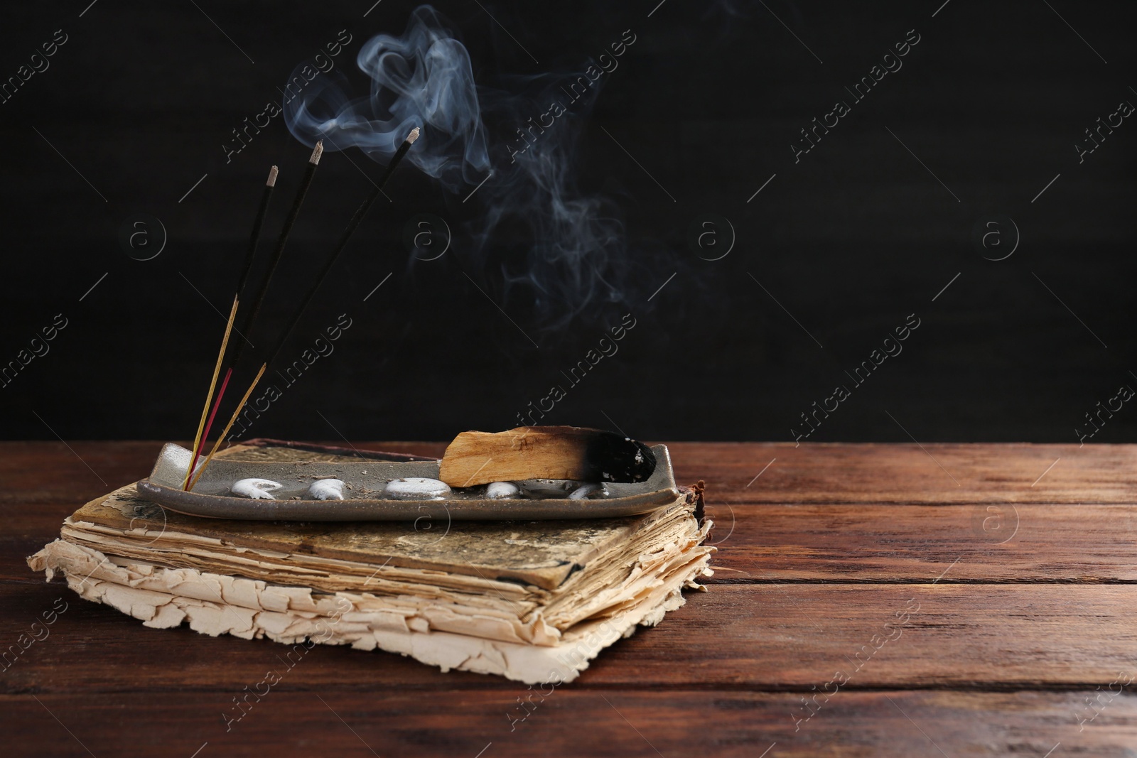 Photo of Aromatic incense sticks smoldering on wooden table. Space for text