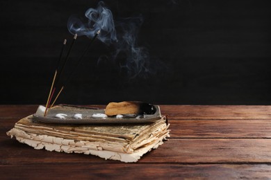 Photo of Aromatic incense sticks smoldering on wooden table. Space for text