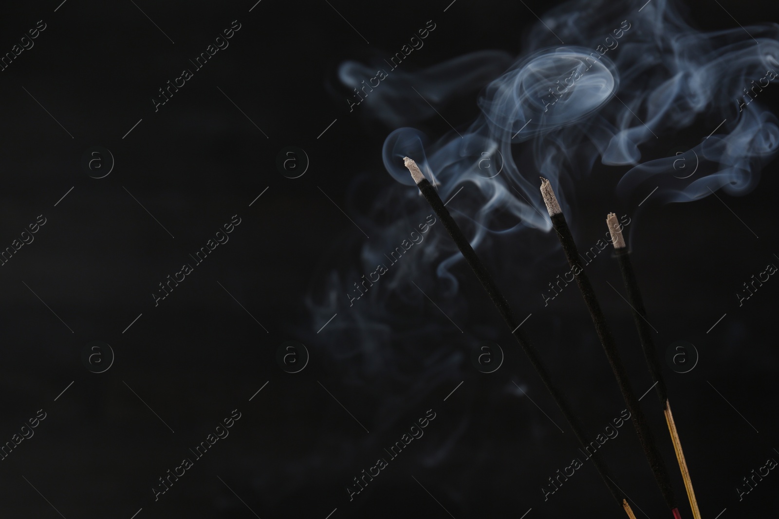 Photo of Aromatic incense sticks smoldering on black background, closeup. Space for text