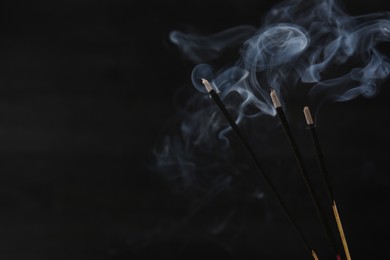 Aromatic incense sticks smoldering on black background, closeup. Space for text