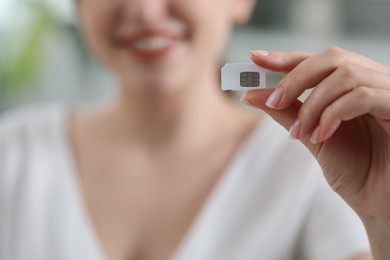 Woman holding SIM card indoors, closeup view