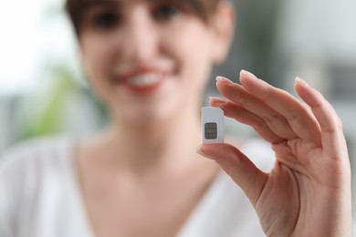 Photo of Woman holding SIM card indoors, selective focus