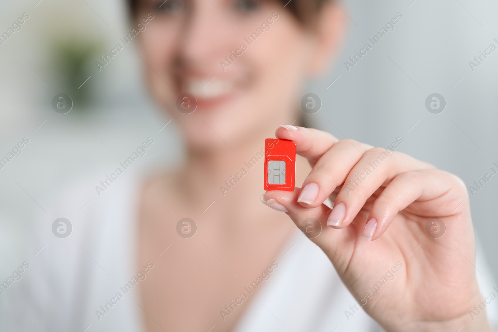 Photo of Woman holding SIM card indoors, selective focus