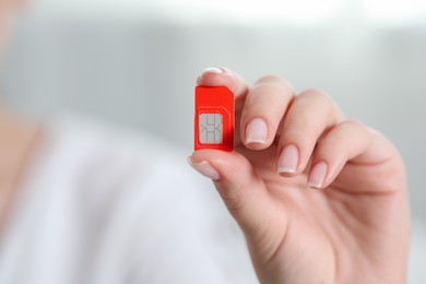 Woman holding SIM card indoors, closeup. Space for text