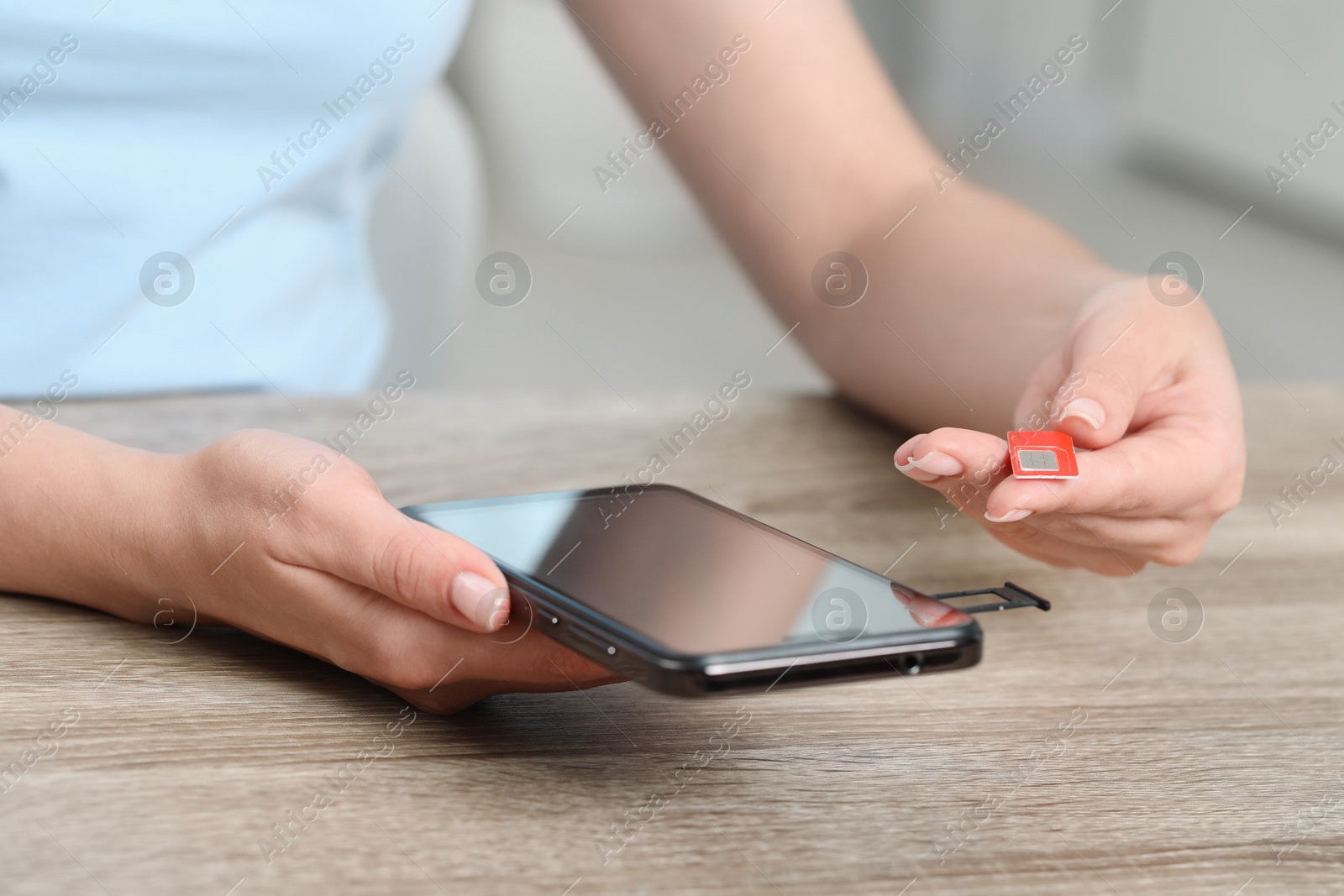 Photo of Woman holding SIM card and smartphone at wooden table indoors, closeup