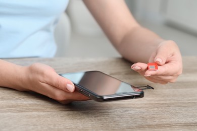 Woman holding SIM card and smartphone at wooden table indoors, closeup