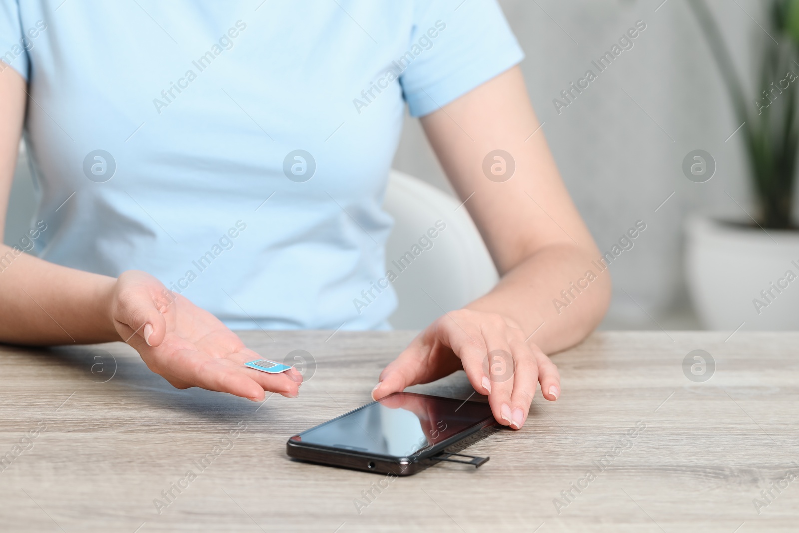 Photo of Woman holding SIM card near smartphone at wooden table indoors, closeup