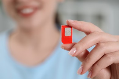 Woman holding SIM card at home, closeup view