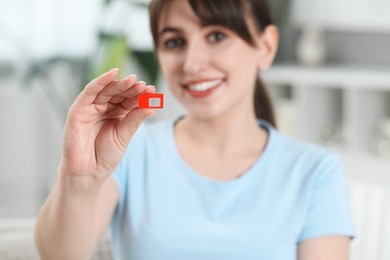 Woman holding SIM card at home, selective focus