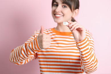 Woman with SIM card showing thumbs up on pink background, selective focus