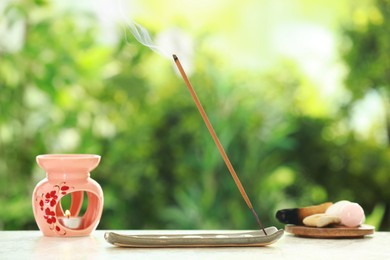 Incense stick smoldering in holder and stones on light table outdoors