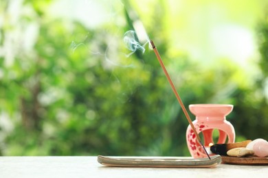 Photo of Incense stick smoldering in holder and stones on light table outdoors, space for text