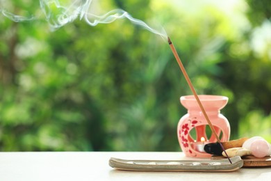 Photo of Incense stick smoldering in holder and stones on light table outdoors, space for text