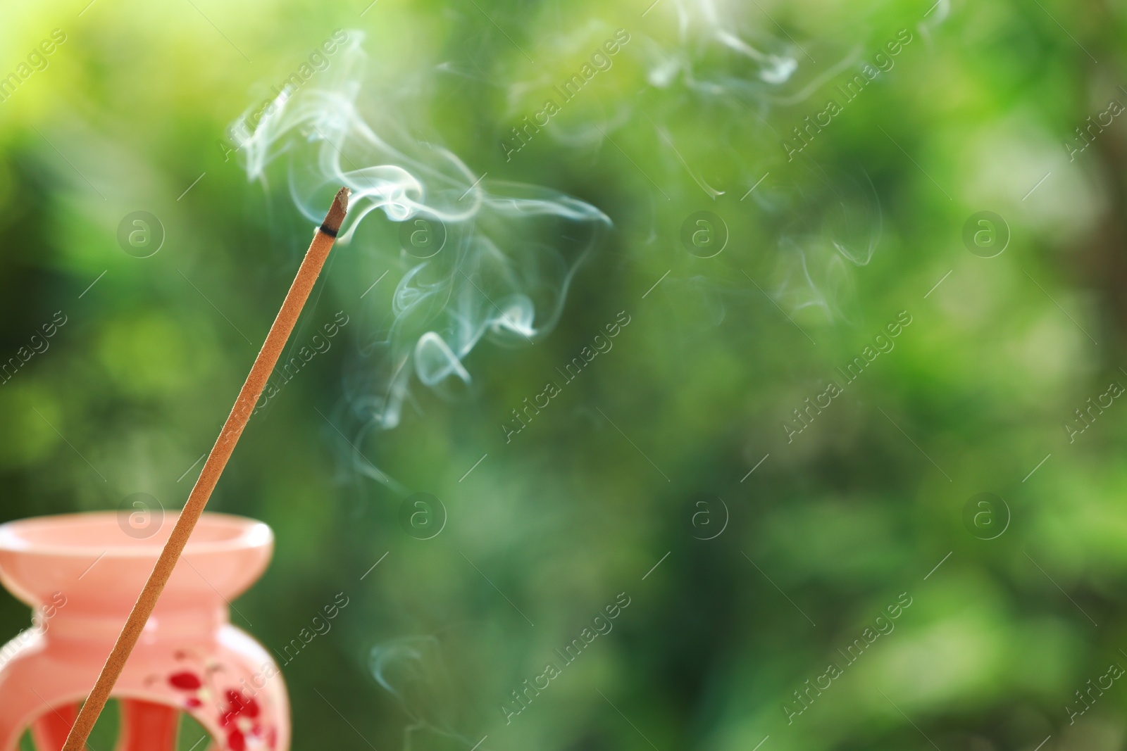 Photo of Incense stick smoldering near holder against green blurred background, space for text