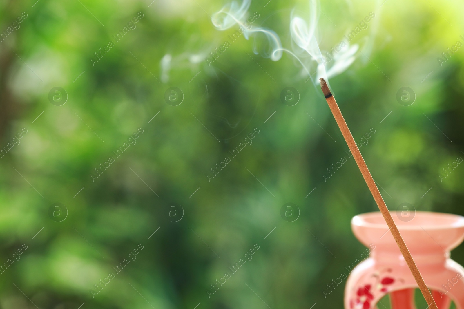 Photo of Incense stick smoldering near holder against green blurred background, space for text