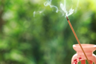 Photo of Incense stick smoldering near holder against green blurred background, space for text