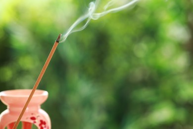 Photo of Incense stick smoldering near holder against green blurred background, space for text