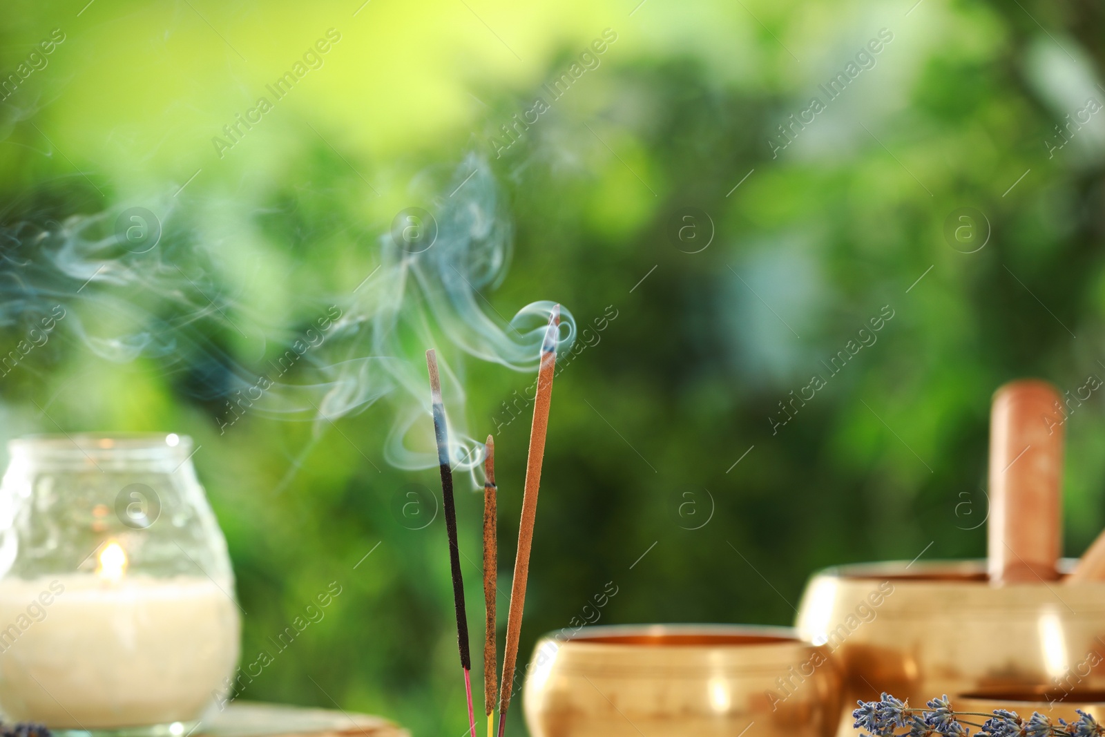 Photo of Incense sticks smoldering near Tibetan singing bowls and candle against green blurred background