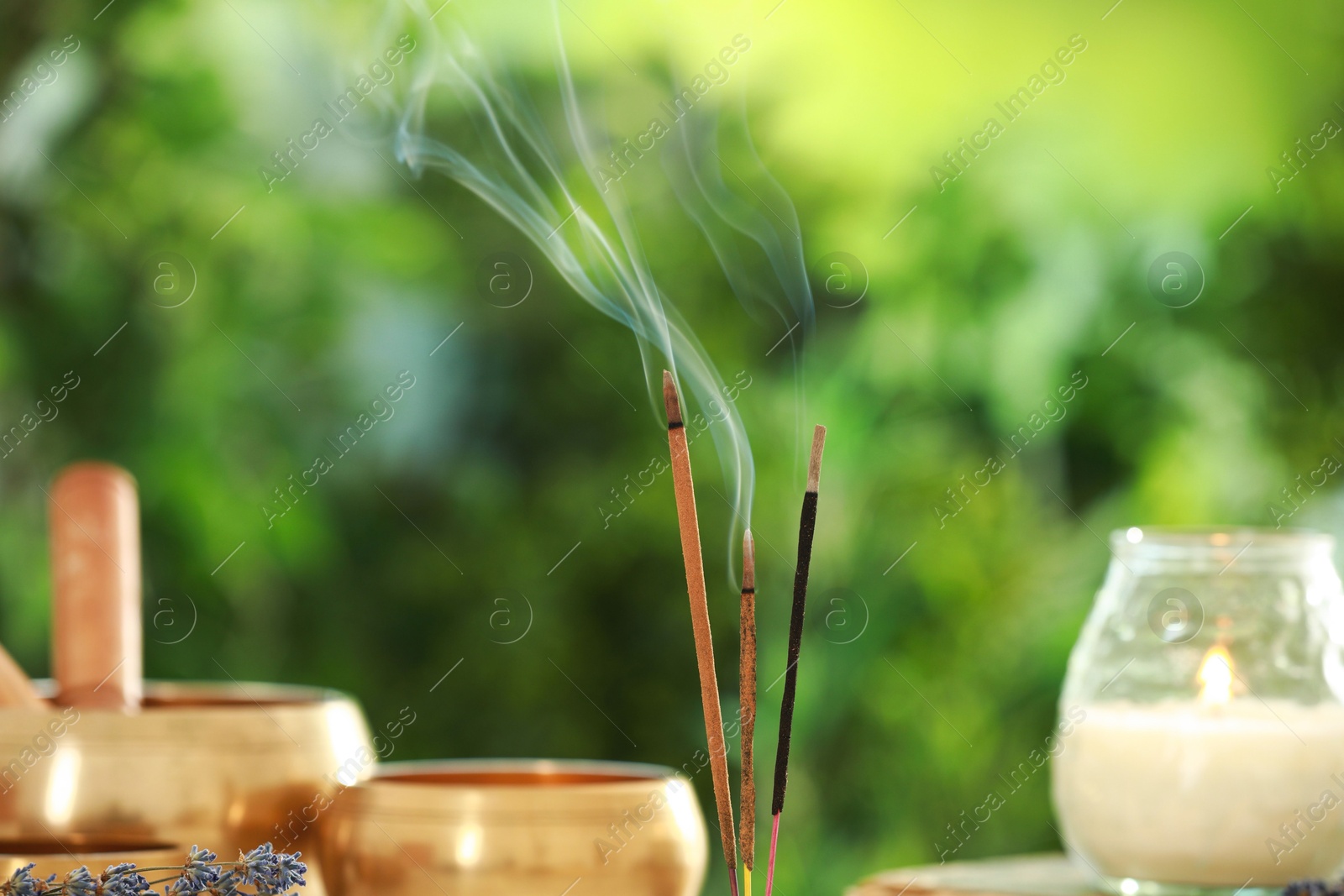 Photo of Incense sticks smoldering near Tibetan singing bowls and candle against green blurred background