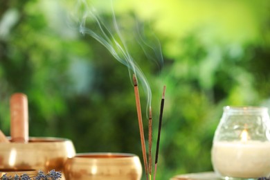 Incense sticks smoldering near Tibetan singing bowls and candle against green blurred background