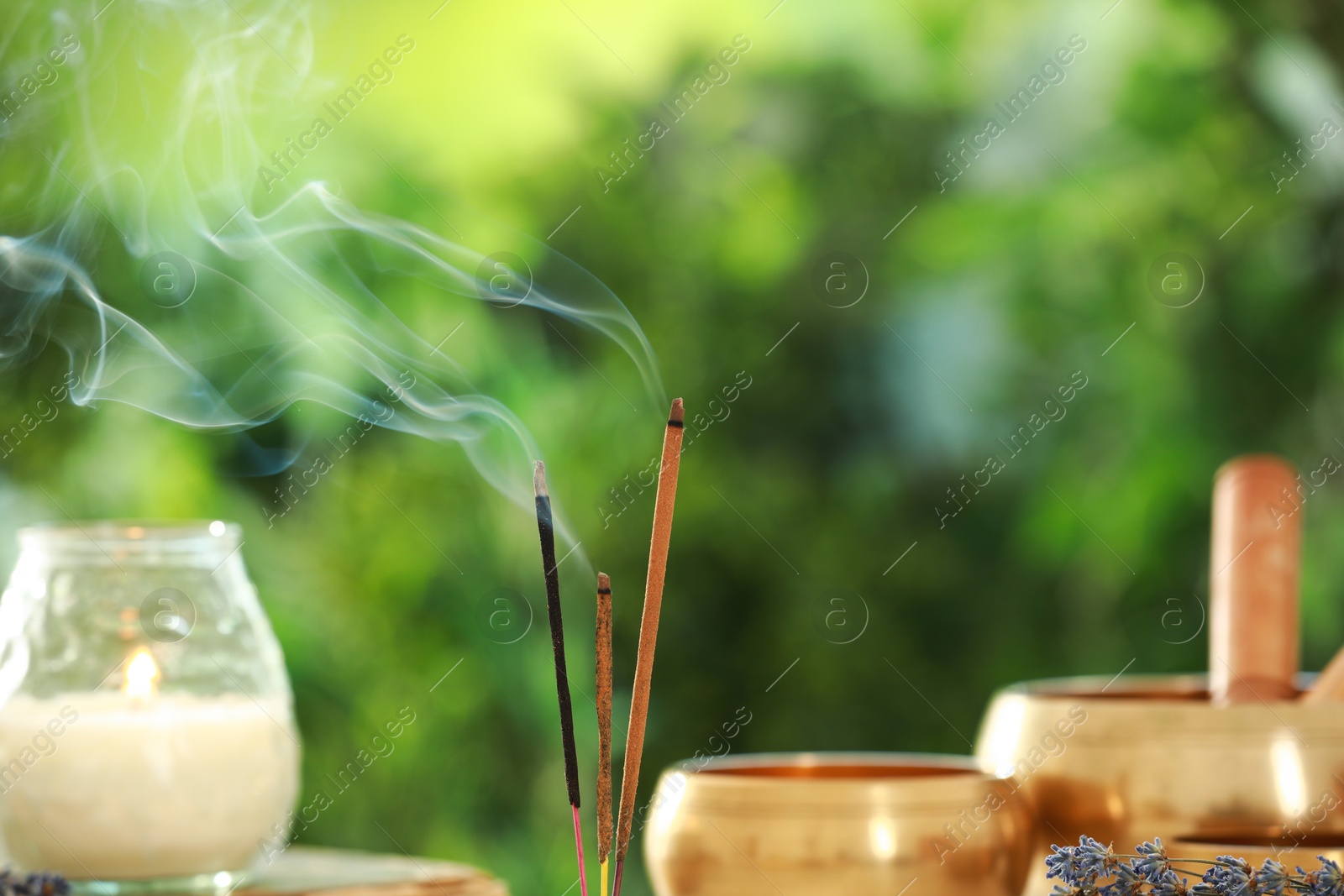 Photo of Incense sticks smoldering near Tibetan singing bowls and candle against green blurred background