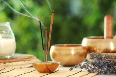 Photo of Incense sticks smoldering in holder, Tibetan singing bowls, dried lavender and candle on table outdoors