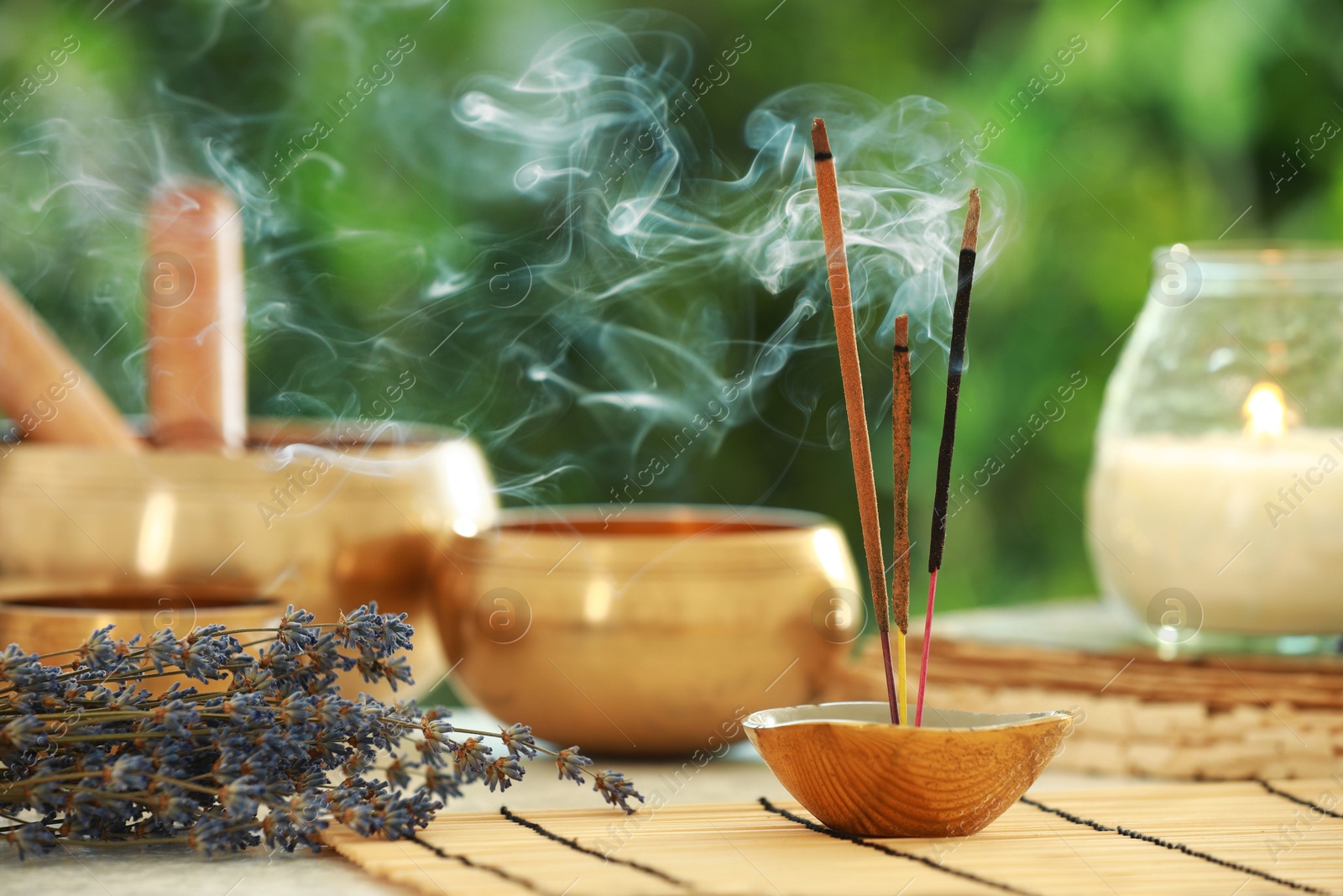 Photo of Incense sticks smoldering in holder, Tibetan singing bowls, dried lavender and candle on table outdoors