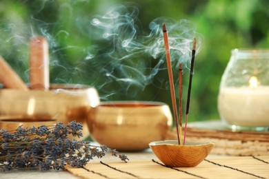 Incense sticks smoldering in holder, Tibetan singing bowls, dried lavender and candle on table outdoors