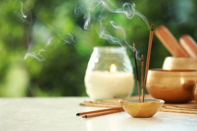 Photo of Incense sticks smoldering in holder, Tibetan singing bowl and candle on light table outdoors, space for text