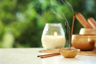 Photo of Incense sticks smoldering in holder, Tibetan singing bowl and candle on light table outdoors, space for text