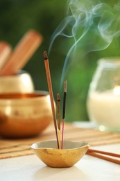 Photo of Incense sticks smoldering in holder, Tibetan singing bowl and candle on light table outdoors