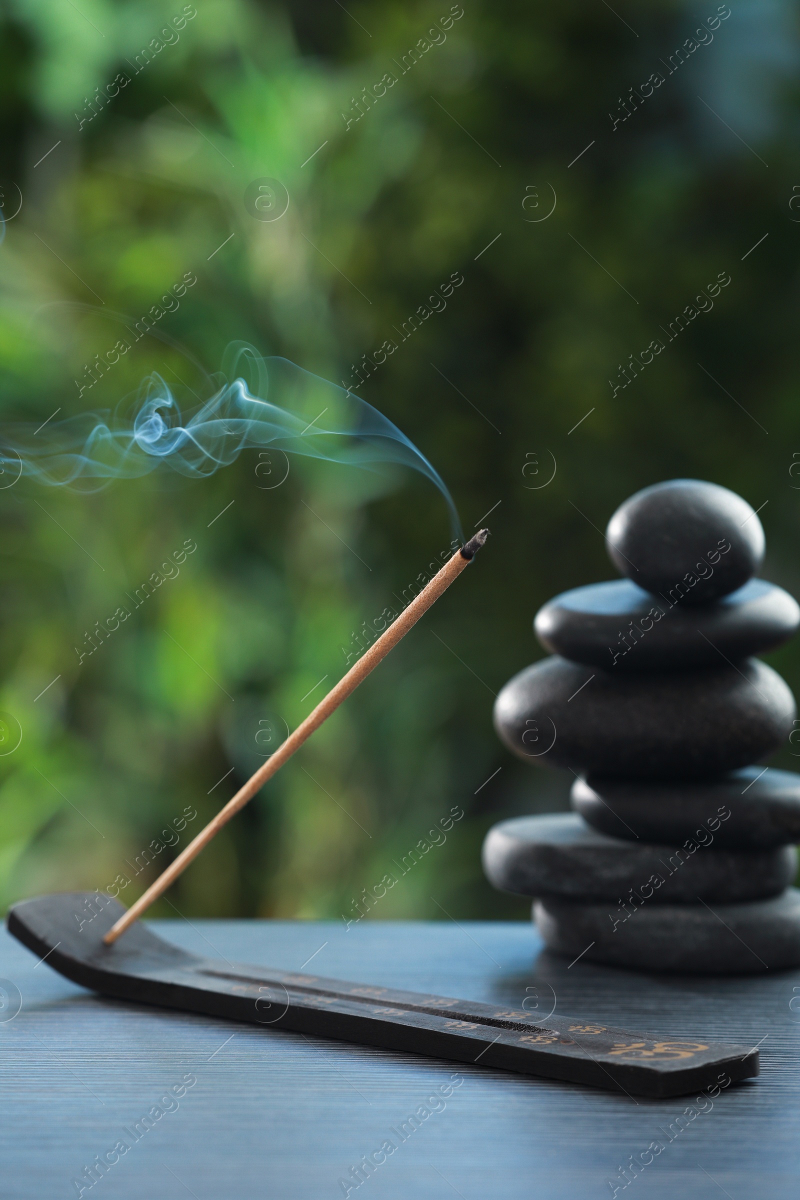 Photo of Incense stick smoldering in holder and spa stones on wooden table outdoors. Om ligature