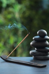 Photo of Incense stick smoldering in holder and spa stones on wooden table outdoors. Om ligature