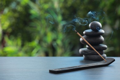 Photo of Incense stick smoldering in holder and spa stones on wooden table outdoors, space for text. Om ligature